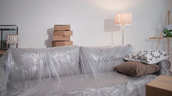 Room After Moving Furniture Covered with Plastic Wrap and Lot of Cardboard Boxes in an Empty