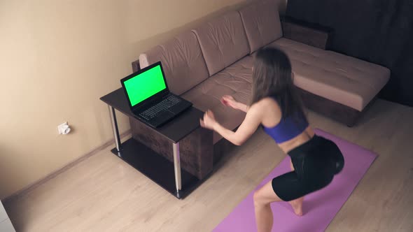 Remote training at home. Athletic woman engaged in fitness online using laptop with green screen alt
