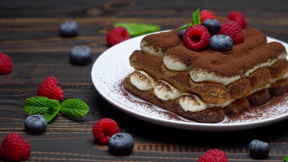 Portion of Classic Tiramisu Dessert with Raspberries and Blueberries on Wooden Background alt