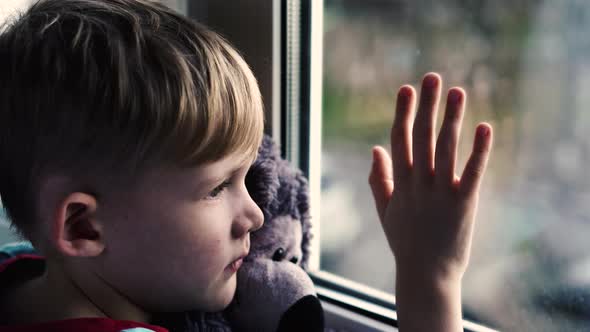 Sad Little Boy Lonely Child With Bear Near Looking Through Window The Little Child Boy is Depressed