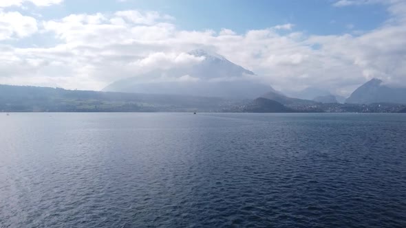 Drone flight over lake thun to the beautiful snow-covered niesen, with a few clouds in the blue sky alt