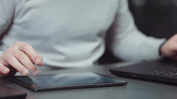 Hands of Businessman Swiping Tablet and Typing on Laptop in Office alt