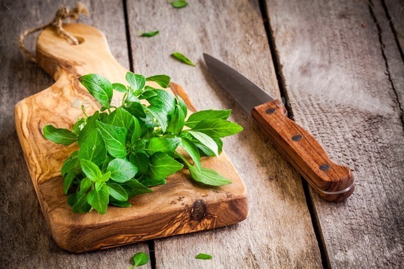 bunch of fresh organic basil in olive cutting board with knife