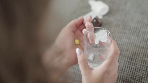 Top Angle View of Female Young Hands Holding Yellow Pill and Glass of Water. Unrecognizable Plus alt