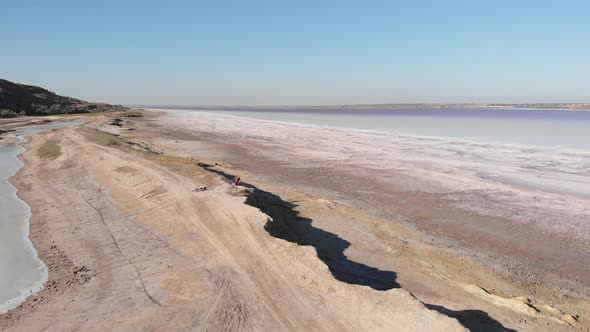 Bike rider is sitting on the edge of seashore of salty lake with pink water Kuyalnik alt