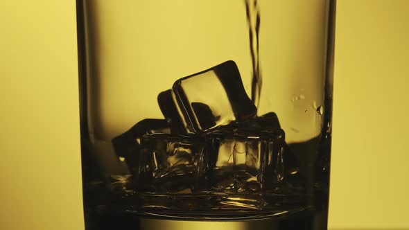 Glass with Whiskey at Yellow Background. Close-up of Whiskey with Ice. alt