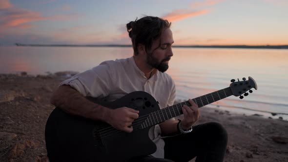 Silhouette of a Young Man Sitting on the Beach By the Water Playing Guitar alt