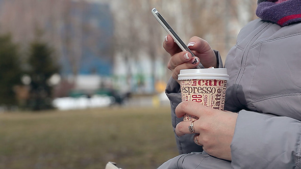 Woman with Coffee Typing Text Message on Phone alt