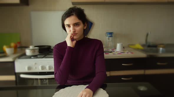 Portrait of a Pretty Brunette Girl in the Kitchen at the Table Sits Thinking alt