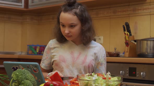 Teen Girl Preparing Salad Looks at the Video Recipe on a Digital Tablet