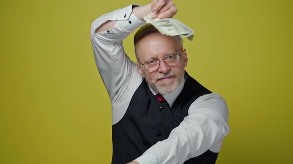 Excited mature man with dollars in hands. Happy elderly man is waving many dollar bills alt