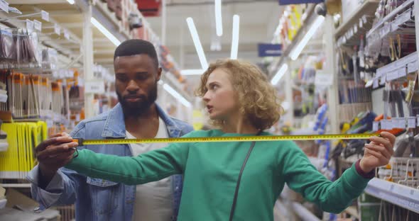 Multiethnic Couple Discuss Measurement with Measure Tape Standing in Hardware Store alt