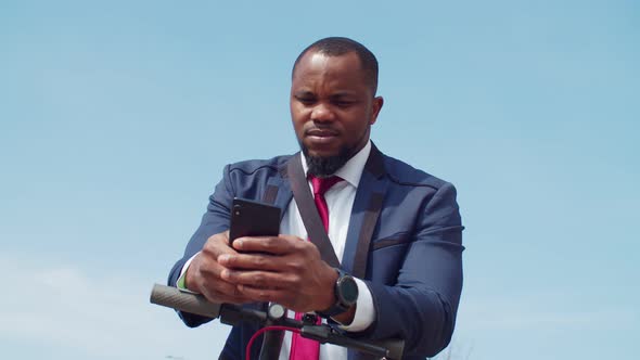Confident Black Businessman on Escooter Using Cellphone alt