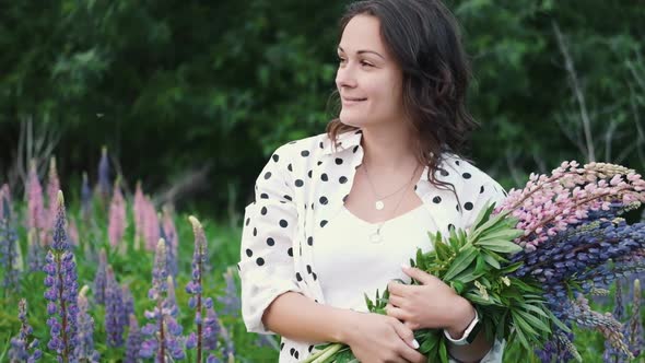 Young Beautiful Woman Posing in a Field with a Bouquet of Lilac Flowers. Happy Brunette in a Field alt
