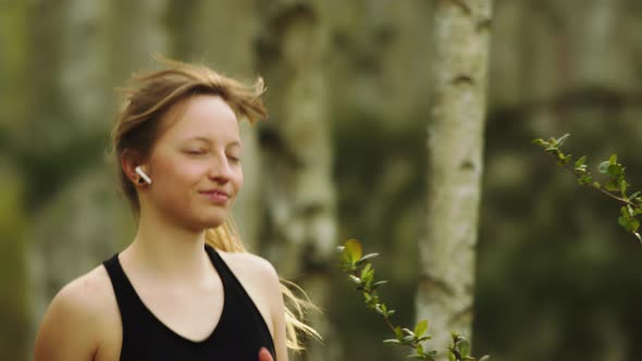 Healthy Lifestyle. Young Caucasian Woman with Wireless Headphones Running in the Forest. Portrait alt