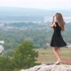 Long haired young woman in short black dress standing on hill top enjoying warm summer day.