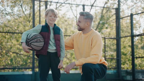 Dad Hugs His Son on at Basketball Court and They Look at the Camera