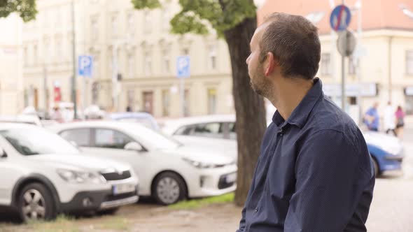 A Caucasian Man Looks Around in an Urban Area  a Colorful Street and Cars in the Blurry Background