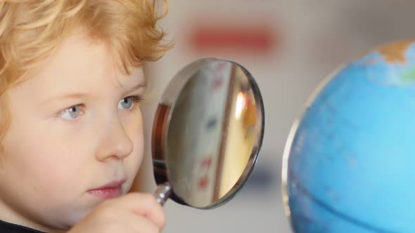 Little blonde boy exploring globe with magnifying glass