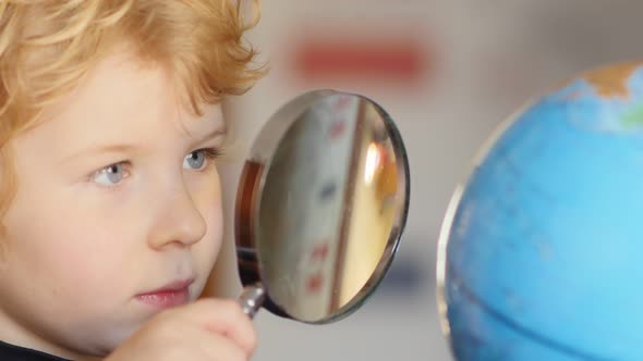 Little blonde boy exploring globe with magnifying glass, Stock Footage