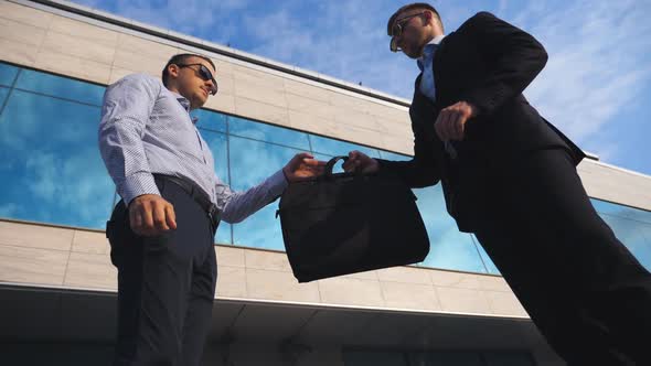Successful Businessman Passing a Black Briefcase To His Partner Near Office Building. Young Male alt