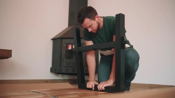 Young Man Assembling Leg Of DIY Table On The Floor. - wide shot alt