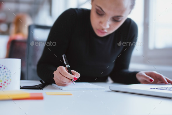 Young woman at her desk taking note - Stock Photo - Images