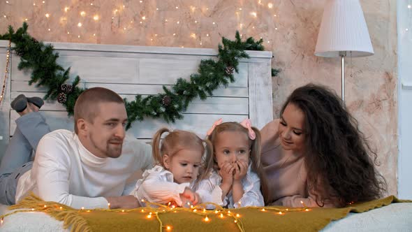 Happy Family with Two Kids Lying Together on Bed at Christmastime alt