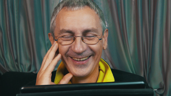 Laughing Man in Glasses Reading a Tablet alt