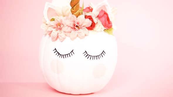 White unicorn pumpkin decorated with flowers on a pink background. alt