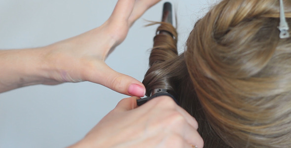 Hairdresser Twists Hair With a Curling Iron