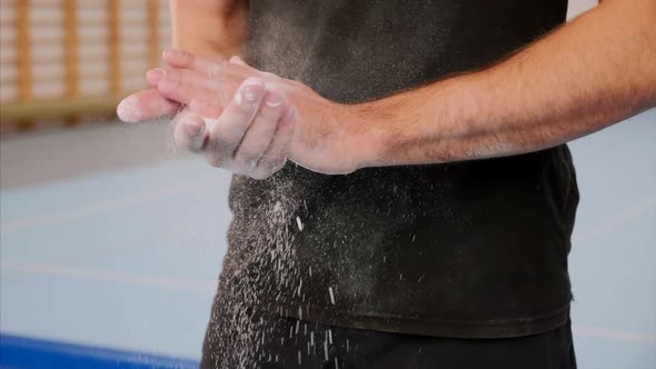 A sportsman is dusting hands with sport magnesia, close-up of arms, slow motion.