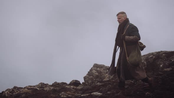 Man In Greatcoat Walking Through Misty And Rocky Landscape alt