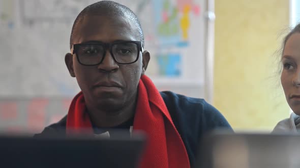 Multiethnic Man and Woman Are Talking and Using Laptops at Workplace in Modern Office Irrl. alt