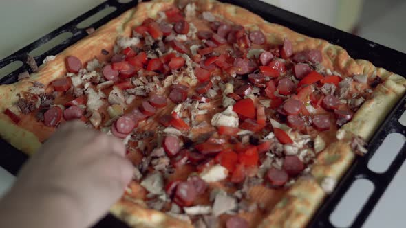 Housewife throws grated cheese on cooked homemade pizza on oven tray at table.