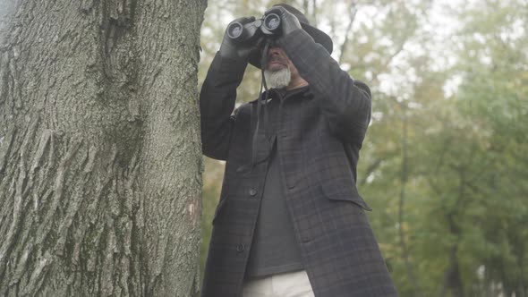 Middle Shot of Concentrated Serious Detective or Intelligence Agent Using Binoculars for Spying alt