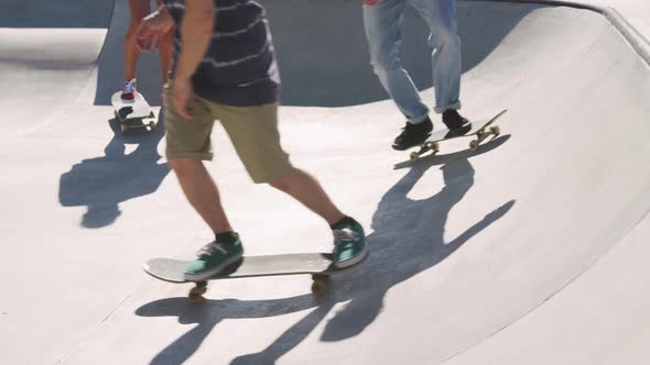 Low section of caucasian woman and two male friends skateboarding on sunny day alt