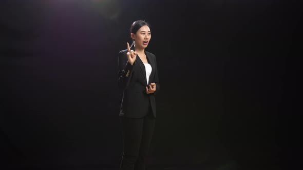 Asian Speaker Woman In Business Suit Holding Her Hands Together While Speaking In The Black Studio alt
