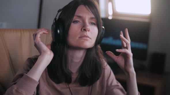A beautiful girl with big headphones listens to music in a chair at the computer, dances, equalizer