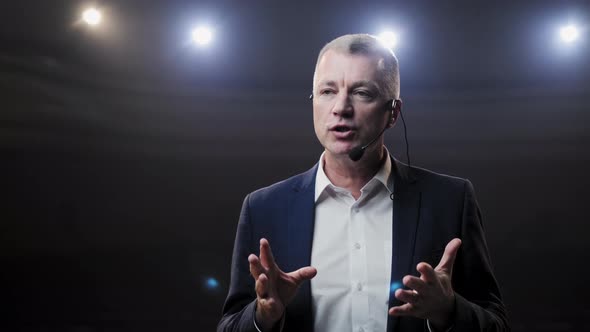 Portrait of Men Speaking Through a Microphone in Dark Conference Hall. Person Says About Marketing alt