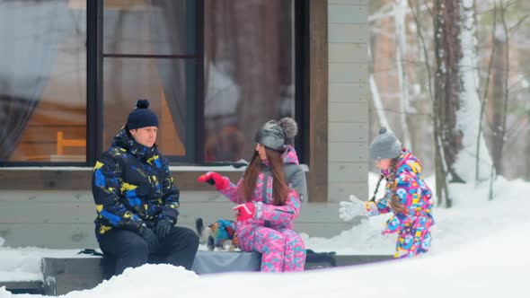 Family with Girl and Dog Sits By Cottage in Winter Forest alt
