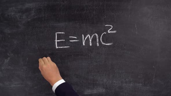 The teacher's hand writes the formula E=mc2 on the blackboard alt