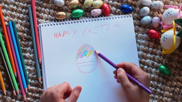View from above as a child draws Easter drawings on the floor in a notebook