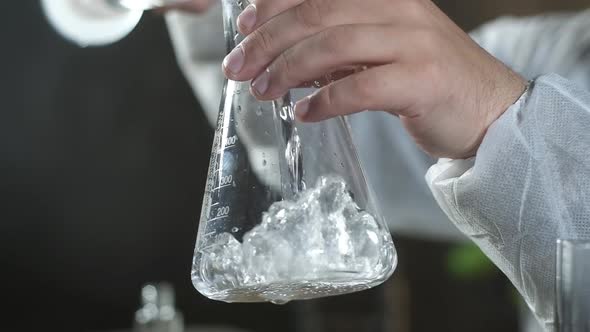scientist in chemical laboratory pours clear solution from test tube into beaker alt