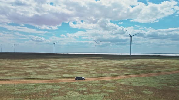 Car Moving By Rustic Road on Wind Electric Generators Background alt