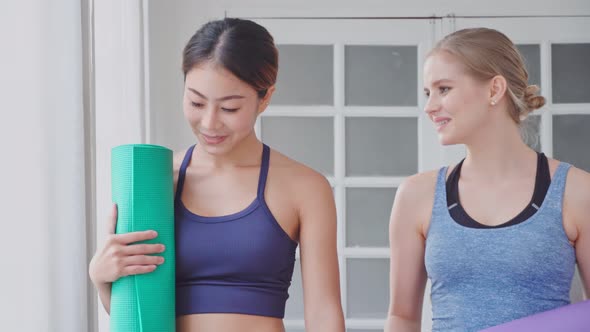Two woman holding yoga mat walk and talk together