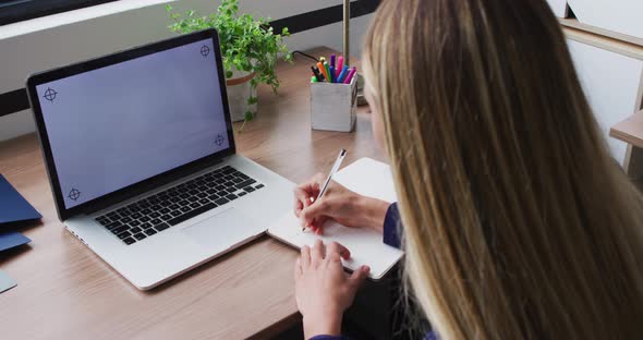 Caucasian businesswoman taking notes during video call, using laptop with copy space on screen alt
