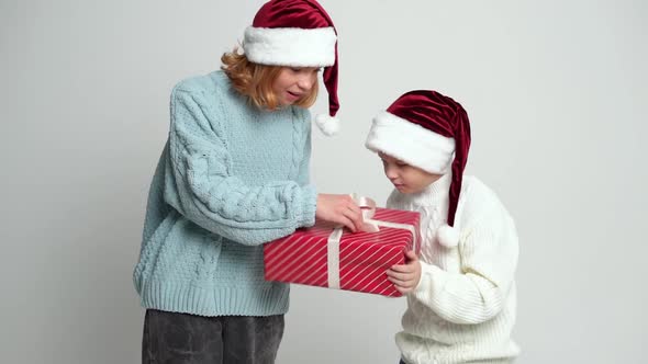 Happy Young Girl and Boy in Santa Claus Caps Opening Present