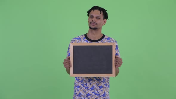 Happy Young Handsome African Man Thinking While Holding Blackboard alt