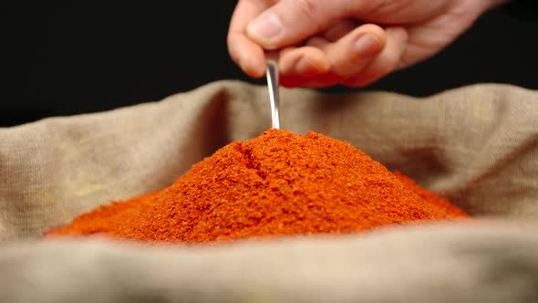 Human hand takes a pinch of a red pepper powder by a spoon from a top of pile in a sac
